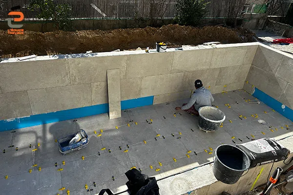 Artisan carreleur de l'Équipe Travaux en train de pose un carrelage de piscine en granit bleu du Brésil