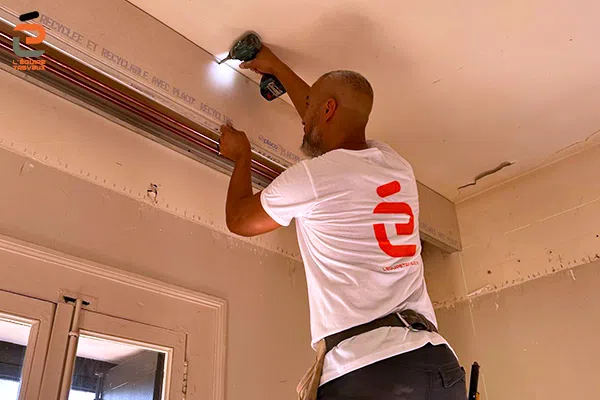 Plaquiste de l'Équipe Travaux en train de fixer une plaque de placoplatre pour habiller des tuyaux de plomberie